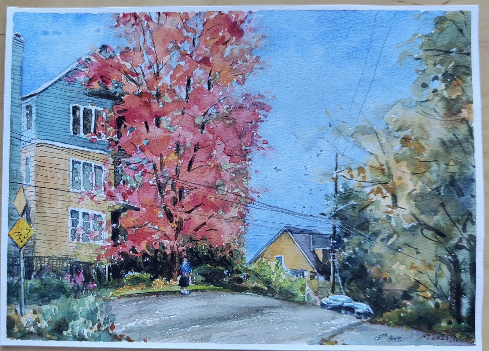 Watercolor of a blazing red maple beside a pale blue house on a quiet street