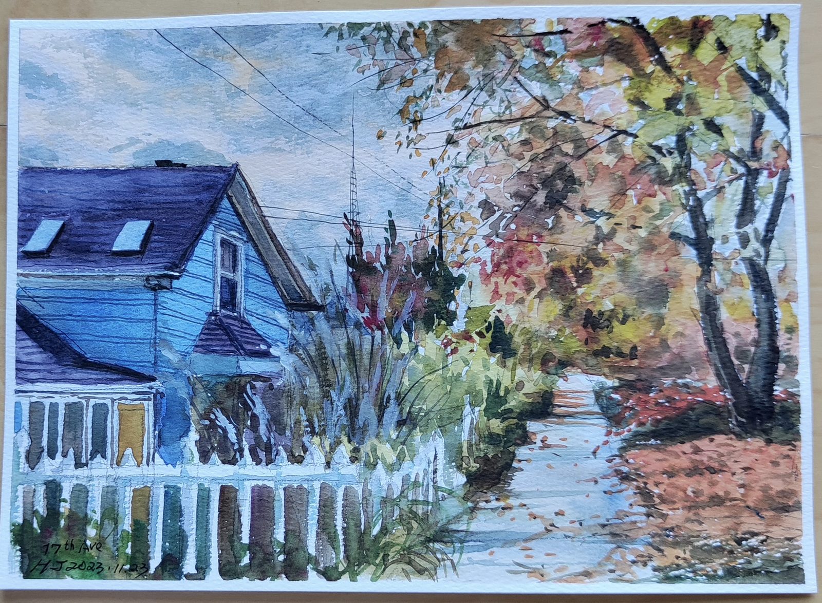 Watercolor of a blue house with a white picket fence under autumn trees